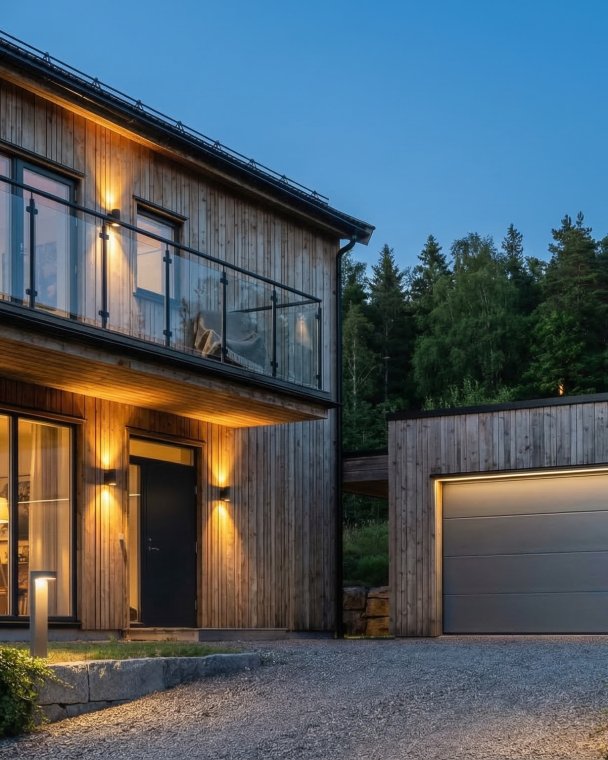 Et moderne trehus med stor balkong og tilhørende garasje, omgitt av natur og skog, perfekt for bolig i naturskjønne omgivelser.