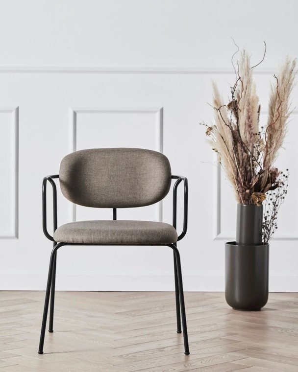 Stol i minimalistisk stue med enkel design og komfortabel polstring, plassert ved siden av en dekorativ vase med tørkede blomster.